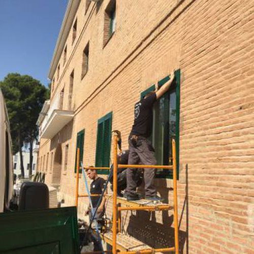 Trabajador en andamio colocando persianas en piso bajo