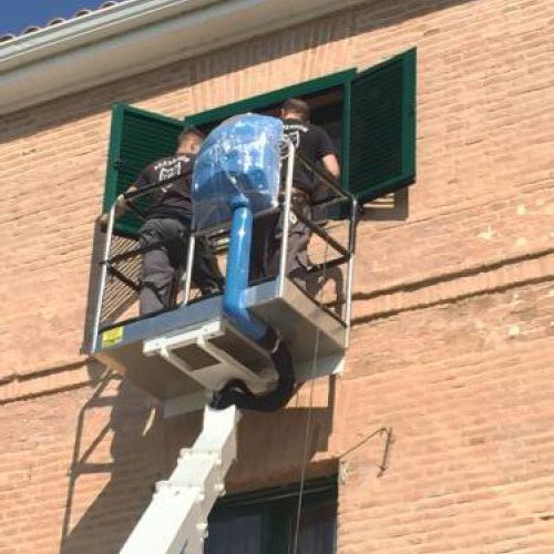 Trabajador subido a grúa colocando persianas en piso superior